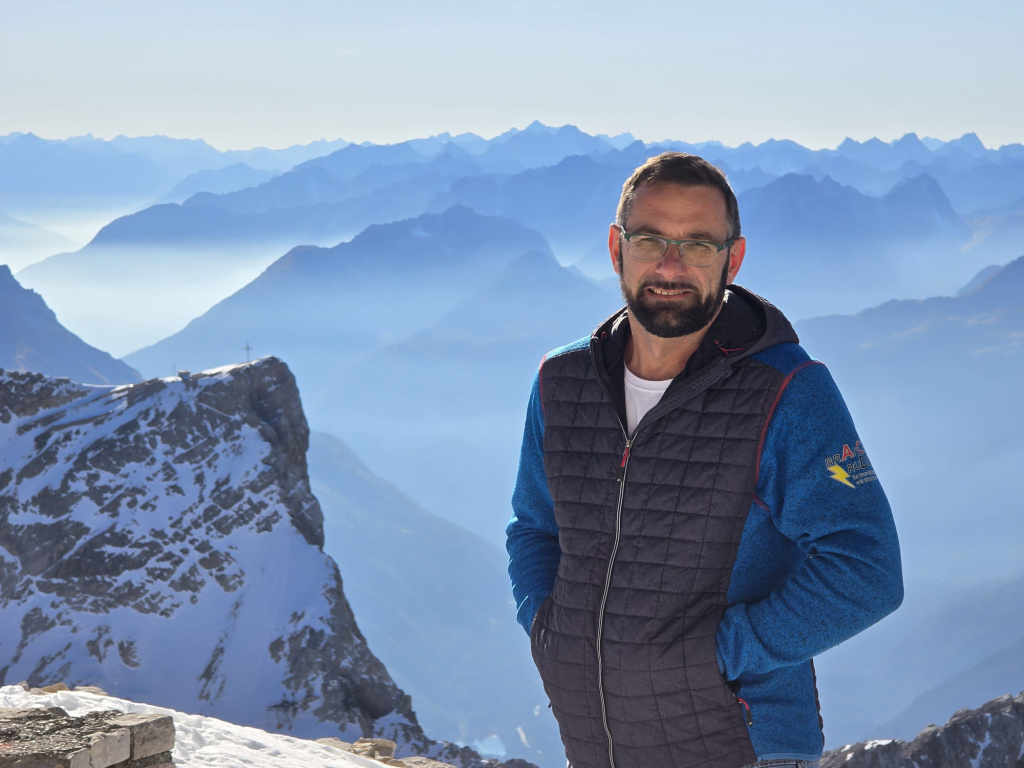 Mann mit Brille steht vor verschneiten Alpenbergen